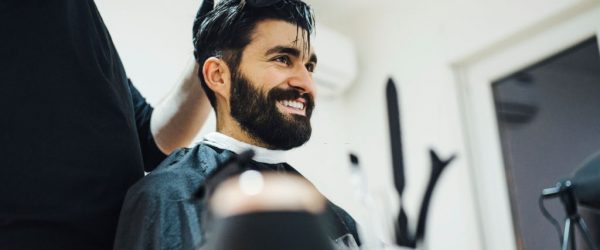 Young stylish barber with mustache and tattoos giving man haircut