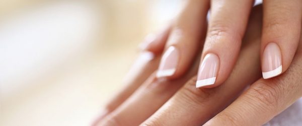 Closeup of nicely manicured female fingernails. One hand is placed on top of other, both on a white towel. Very nice french manicure with transparent nail paint. Blurry beige background. Copy space.
